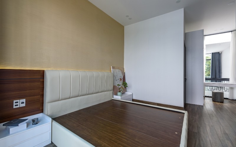 Giường ngủ lớn và êm ái, kết hợp với màu sắc nhẹ nhàng của tường trắng, tạo nên không gian nghỉ ngơi trang nhã và thoải mái